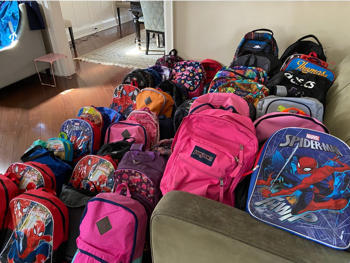 Dozens of backpacks lined up, packed with school supplies